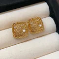 Detaillierte Makroaufnahme von goldenen quadratischen, hohlen Ohrsteckern mit Zirkonia. - Gold