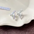 Vista dettagliata di eleganti orecchini a lobo con fiocco bianco su un piatto crema - Orecchini a Bottone a Fiocco / Bianco