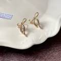 Primo piano di eleganti orecchini a lobo a forma di fiocco dorato su un piatto decorativo - Orecchini a Bottone a Fiocco / Oro