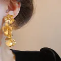 Détail d'élégantes boucles d'oreilles fleuries dorées à trois couches, finition mate - Fleur Dorée (No.3)