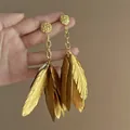 Close-up showing the metallic gold finish and detailed texture of feather earrings - Gold