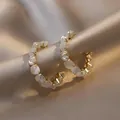 Detailed view of C-shaped gold hoop earrings with white stones and crystals on satin. - Small C-Shaped Hoop