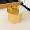 Primer plano de un llamativo brazalete dorado abierto acampanado con acabado mate. - Dorado