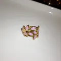 Close-up view of a gold-plated leaf open ring with glittering pink enamel finish details. - Open Style / Purple
