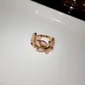 Detailed view of a gold-tone open ring with pink enamel leaf patterns on white base - Open Style / Pink