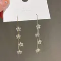Dettaglio ravvicinato di orecchini pendenti a fiori su un cartoncino bianco liscio - Ago D'argento 16# - Ecologico - Oro