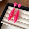 Primer plano de pendientes de gota de acrílico rosa con textura de mármol en bandeja. - Rosa rojo