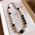 Close-up detail of irregular black and white pearl necklace on a textured jewelry tray - White/Black