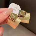 Close-up showing the brushed metal texture and polished finish of the gold square earrings - Gold