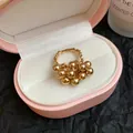Dettaglio di un anello aperto a sfere dorate con fascia testurizzata in una scatola - Stile Perle a Grappolo / Oro