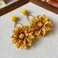 Close-up detail of yellow fabric and raffia flower earrings with elegant golden hooks - Yellow