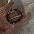 Close-up of oversized matte black geometric hoop earrings held in hand for scale - Geometric Plain Ring Style (HE6491) / Black