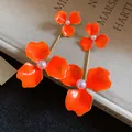 Detaillierte Nahaufnahme der orangefarbenen Blumenohrringe mit eleganter Perlenmitte - Blumenanhänger-Stil / Orange