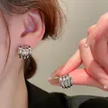 Detailed close-up view of silver-toned ribbed hoop earrings worn on a model's ear - Style 32 / Silver