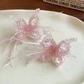 Detailansicht von rosa Kristall-Schmetterlingsschmuck mit Federn auf einem cremefarbenen Teller - Clip-Ohrringe / Rosa