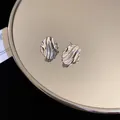 Minimalist silver irregular textured wavy oval stud earrings displayed on mirror surface - Style 37 / Silver