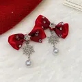 Detailed view of red bow earrings with sparkling snowflake dangles and white pearls. - Earrings / Red