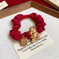 Détail d'un chouchou en tissu rouge orné d'un pendentif en forme de cheval doré. - Cheval de bon augure - Classique / Rouge