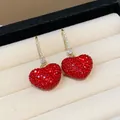 Close-up view of elegant red crystal heart earrings with sparkling zircon paved hooks - Gold Ear Hook / Red