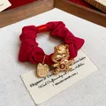 Vue détaillée d'un chouchou rouge avec une breloque cheval dorée et étiquette. - Cheval de bon augure - Bonheur / Rouge