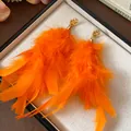 Close-up of vibrant orange feather tassel earrings with gold textured studs on a white tray. - Gold Orange