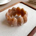 Dettaglio macro di un bracciale in grani di acrilico marmorizzato marrone su vassoio beige - Caffè Scuro