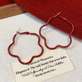 Detail view of red flower-shaped hoop earrings with elegant matte finish on canvas - Red