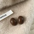 Detail of brown glossy oval resin stud earrings on soft beige fur background - Oval Teardrop / Dark Coffee