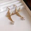 Primo piano di orecchini vintage a forma di rondine in oro con eleganti pendenti di perle bianche - Ganci per orecchini / Oro