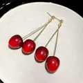 Detail view of red cherry dangle earrings with gold long stems on a white plate. - Cherry Pendant / Red