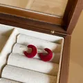 Close-up of elegant red flocking C-shaped stud earrings displayed in a wooden box - Red