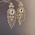 Makroaufnahme von luxuriösen goldfarbenen Kronleuchter-Ohrringen mit Strass-Fransen. - Gold