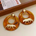 Vista dettagliata di orecchini a cerchio in resina ambrata con una tigre dorata. - Cerchio di Tigre (HE22312) / Perno per orecchini in argento-Oro-Caffè