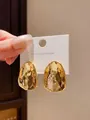 Close-up of irregular gold-tone hammered metal stud earrings on white display card - Irregular Geometric / Gold