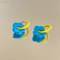 Orecchini a fiore blu vibrante con cerchi gialli su una superficie riflettente pulita. - Cerchio a Contrasto Giallo Blu