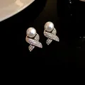 Macro view of French retro earrings featuring large pearl and rhinestone cross base detail - Stud Earrings / Gold-White