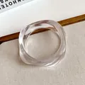 Close-up of a clear acrylic bangle with an irregular wavy design on a textured surface. - White