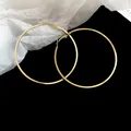 Detailed macro view of large gold-toned minimalist hoop earrings on a black background - Style 57 / Diameter 50mm / Gold