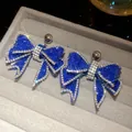 Close-up of sparkling blue rhinestone bow earrings on a grey velvet jewelry tray. - Silver Blue (20#)