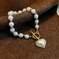 Gros plan d'un élégant bracelet de perles blanches avec fermoir OT doré et pendentif coeur - Blanc