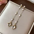 Dettaglio macro di eleganti orecchini lunghi pendenti in oro con perle bianche e vetro - Oro Bianco