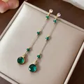 Vista dettagliata di eleganti orecchini pendenti dorati con pietre di vetro verde smeraldo - Oro Verde