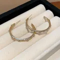Close-up of gold-plated hoop earrings with sparkling zircon stones and cross pattern - C-Shaped Cross Style / Gold