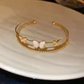 Primer plano detallado de un brazalete de oro de dos capas con circonitas y dijes de mariposa - Estilo Mariposa Doble Hueca / Dorado
