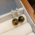 Dettaglio ravvicinato di orecchini dorati con zirconi e pietre occhio di tigre. - HE29368 (Stile Ago d'Argento) / Oro/Marrone