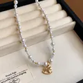 Close-up detail of an elegant pearl necklace featuring a gold rocking horse pendant - White