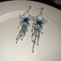 Dettaglio degli orecchini a farfalla in argento con cristalli blu su un piatto di ceramica. - Stile Farfalla Nappina / Un paio / Blu