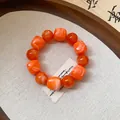 Close-up of orange acrylic beaded bracelet with irregular geometric charms on fabric - Orange