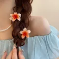 Set of two orange plumeria flower hair claw clips demonstrated on a braided hairstyle - One Pair / Orange Gradient Pair
