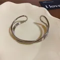Primo piano dettagliato di un bracciale rigido aperto a strati incrociati in argento. - Stile incrociato multistrato / Argento